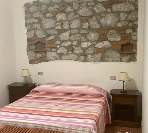 1 dormitorio con cama y pared de piedra en PODERE OSLAVIA AZ.AGR.BIO GIANNINI, en Alberese