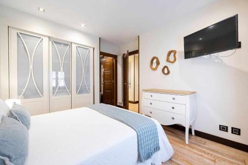 a bedroom with a white bed and a tv on the wall at Apartamento Playa de Luanco Lux in Luanco