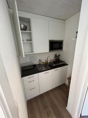 a small kitchen with white cabinets and a sink at ALP APARTMENTS centre location with traditional design and self check-in in Engelberg