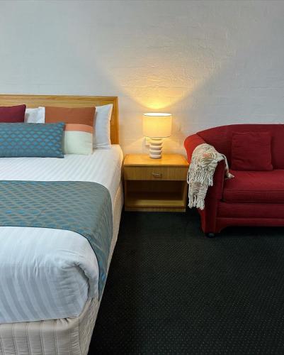 a hotel room with two beds and a red chair at Grand Country Lodge Motel in Mittagong