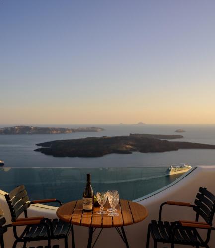 a table with wine glasses on a balcony with a view at Aethria Villa in Imerovigli