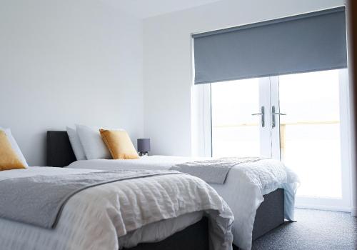 a white bedroom with two beds and a window at Shoreland Lodges - Holly Lodge in Fort Augustus