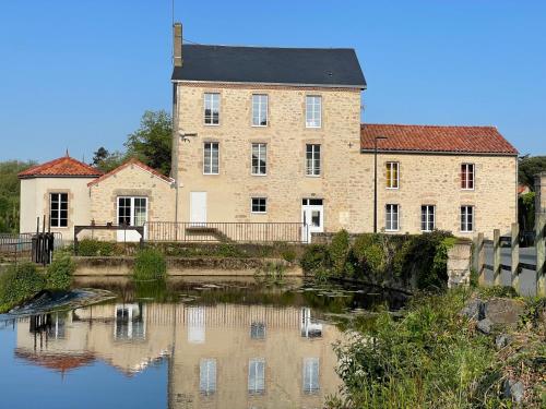 a large brick building next to a body of water at Gîte moulin de Chaussac proche du Puy duFou in Saint-Laurent-sur-Sèvre