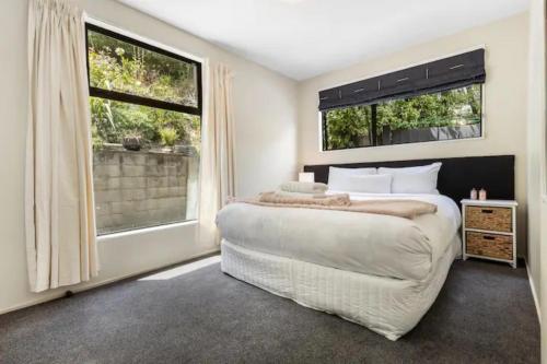 a bedroom with a large bed and two windows at The Alpine - Queenstown Holiday Home in Queenstown