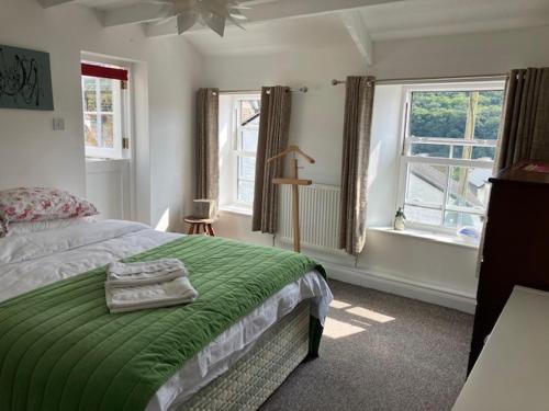 a bedroom with a bed with a green blanket and two windows at Entire characterful cottage in Calstock, Cornwall in Calstock