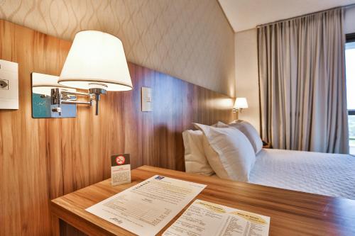 a hotel room with a bed and a desk with a lamp at MG Flats Hotel & Residence in Cuiabá