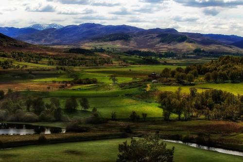 a green field with a river and mountains in the background at Spectacular Mountain View Ecopod in Newtonmore