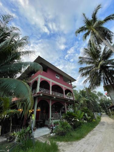 una casa rosa con palmeras delante en Mythai Guesthouse, en Chaloklum