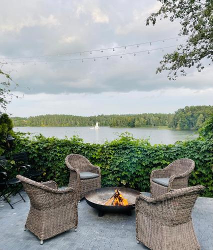 three wicker chairs and a fire pit with a view of a lake at Dom Wiejska 39 a in Ruciane-Nida