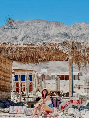 a woman in a hat sitting under a straw hut at New Bella Sina Camp in Nuweiba