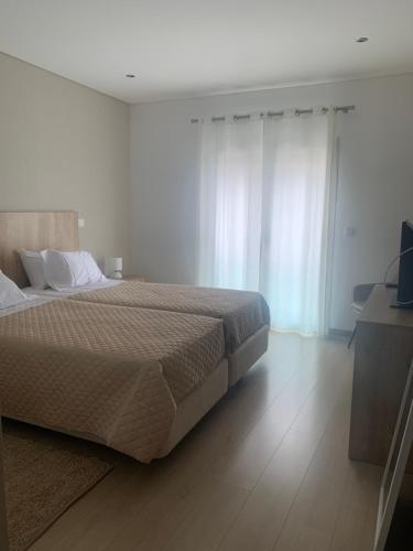 a bedroom with a large bed with white walls and wooden floors at Apartamento Fátima Sanctuary in Fátima