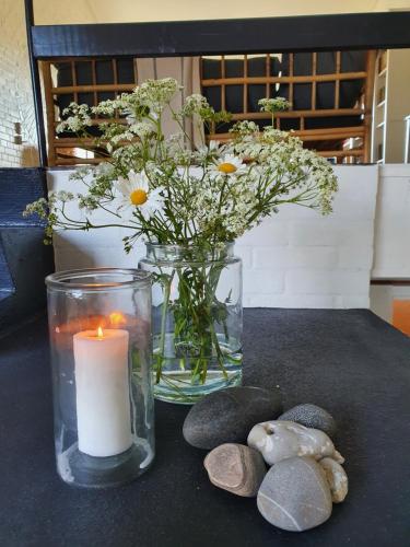 a candle and a vase with flowers and rocks at Sandvighus in Sandvig