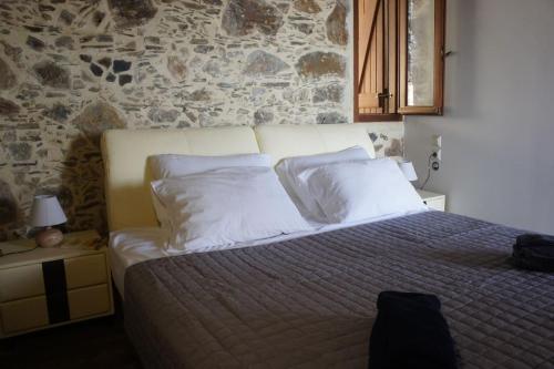 1 dormitorio con 1 cama con almohadas blancas y pared de piedra en Alegria stone house, en AmigdhalokeFálion