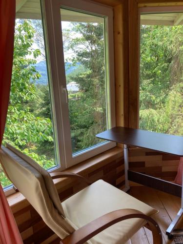 a table and chairs in a room with windows at Хата Різьбяра - Закуток in Beloberëzka