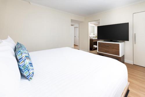 a white bedroom with a large bed and a flat screen tv at The Anza-a Calabasas Hotel in Calabasas