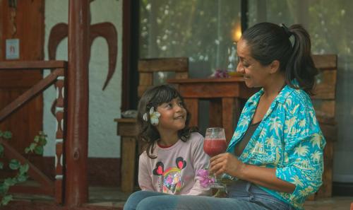 a woman sitting next to a little girl holding a drink at Cabañas MANA NUI INN in Hanga Roa