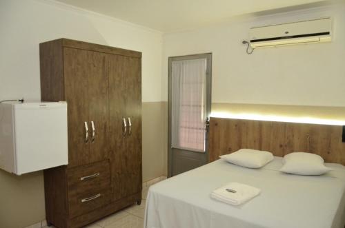 a bedroom with a bed with white sheets and a refrigerator at HOTEL VITORIA REGIA in Engenheiro Beltrão