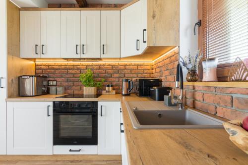 a kitchen with white cabinets and a brick wall at Domki Mazurska Dolina in Mikołajki