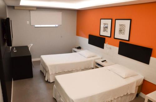 Habitación con 2 camas y pared de color naranja. en Hotel São Domingos en Feira de Santana