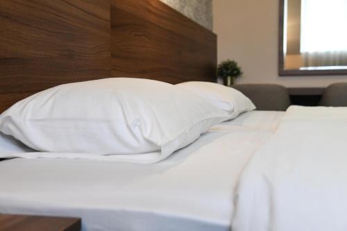 a white bed with white pillows and a wooden headboard at Hotel Garden in Novi Sad