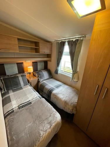 two beds in a small room with a window at Millfields Holiday Park - Diamond Deluxe - Coastal Caravan Breaks in Ingoldmells