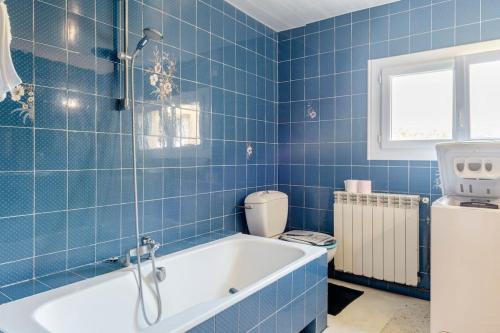 La salle de bains est pourvue de carrelage bleu, d'une baignoire et de toilettes. dans l'établissement Gîte Le Campane - Piscine partagée Borne recharge véhicule 22kwh, à Laujuzan