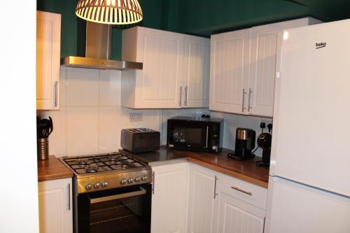 a kitchen with white cabinets and a stove top oven at Cosy Home Ideal for Business, Contractors, Families near Walsgrave Hospital, Shops and M6, A46, Free Parking in Wyken