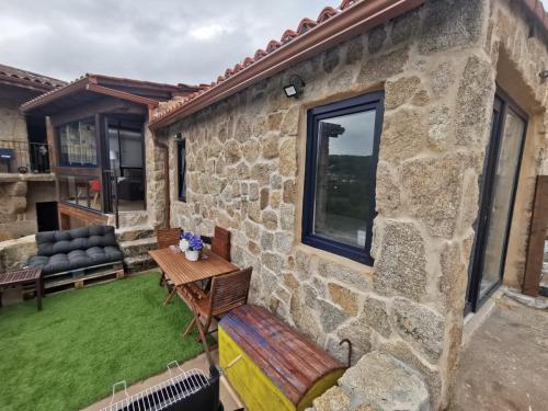 a patio with a table and a bench next to a stone building at O Recuncho de Tibias in Pereiro de Aguiar