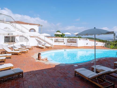 a woman sitting in front of a swimming pool at Hotel Pedra Santa in Baja Sardinia