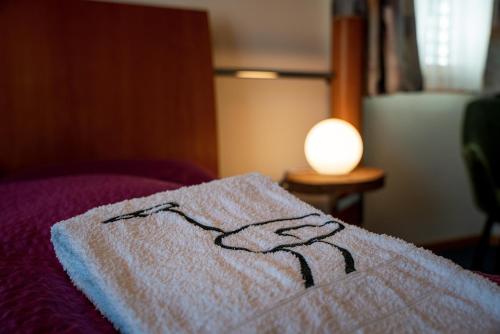 a towel on a bed next to a lamp at Kulinarik & Geniesser Hôtel STRAUSS in Fiesch