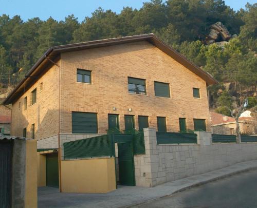 un edificio de ladrillo con puertas verdes y una valla en Apartahotel Rural CollaRubio Luxury, en Collado Mediano