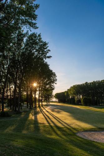 a tree lined road with the sun setting behind it at Greenfield Hotel Golf & Spa in Bük