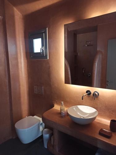 a bathroom with a sink and a toilet and a mirror at Amphitrite Suites Santorini in Vóthon