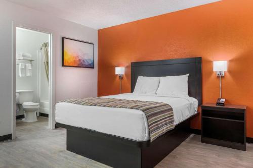 a bedroom with a large bed with an orange wall at Suburban Studios Spartanburg - I-26 in Spartanburg