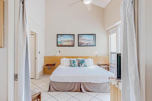 a white bedroom with a bed and a tv at Maui Banyan B204 in Wailea