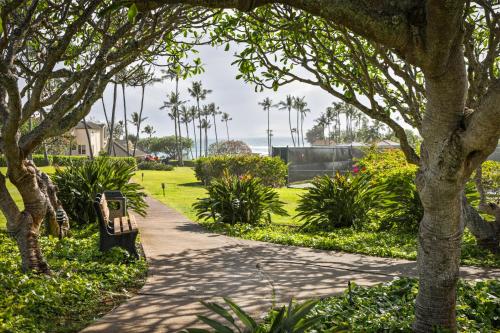 a walkway through a park with trees and a bench at Aston At Poipu Kai in Koloa