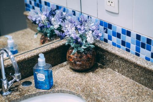 un lavabo con una botella de jabón y flores púrpuras en Flat BOUTIQUE em frente ao metrô MOEMA, en São Paulo