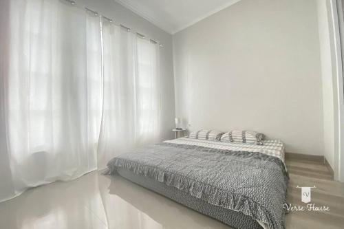 a white bedroom with a bed and white curtains at Verse House in Pontianak