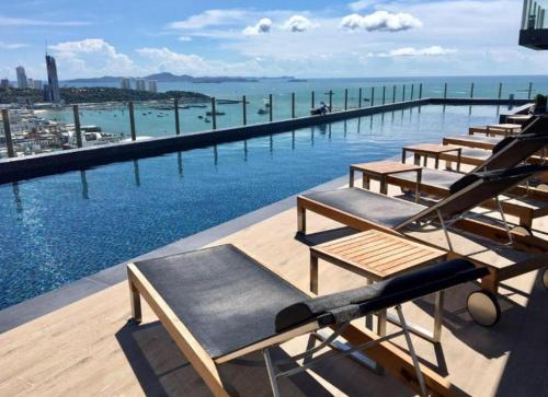 BASE Central PATTAYA Long Balcony with Infinity Pool & Free Netflix! في باتايا سنترال: على صف من كراسي الجلوس فوق حمام السباحة