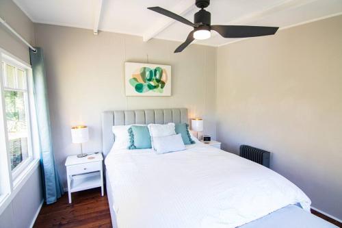 a bedroom with a white bed with a ceiling fan at Banksia Cottage, pretty cottage with garden in Leura