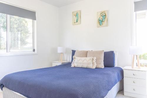a white bedroom with a blue bed with two windows at Nannys Beach House in Berrara