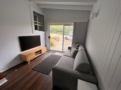 a living room with a couch and a flat screen tv at Sunflower House, a cozy cabin at Lake Wentworth in Wentworth Falls
