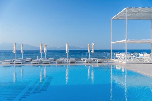 a swimming pool with umbrellas and chairs and the ocean at Dimitra Beach Hotel & Suites in Agios Fokas