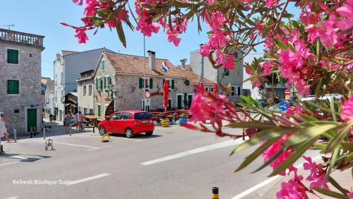 Une voiture rouge descendant dans une rue avec des fleurs roses dans l'établissement Refresh Boutique Suites - Central Point, à Vodice