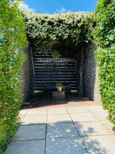 a black bench sitting under a hedge with flowers at B&B Villa degli Angeli in Bernalda