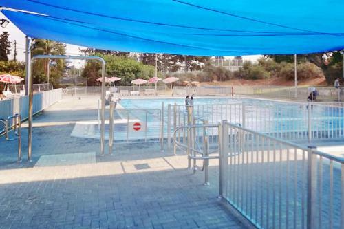 una piscina con sombrilla azul, mesas y sillas en Travel Hotel Gesher Haziv, en Gesher HaZiw