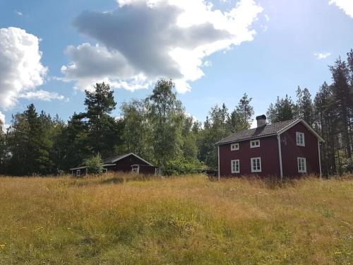 a red barn in the middle of a field at Charmig gård med bastu, strandtomt och utedusch i naturskönt område in Sveg