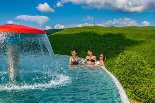 3 Frauen sitzen in einem Pool mit Springbrunnen in der Unterkunft Hotel Ózon & Luxury Villas in Mátraháza