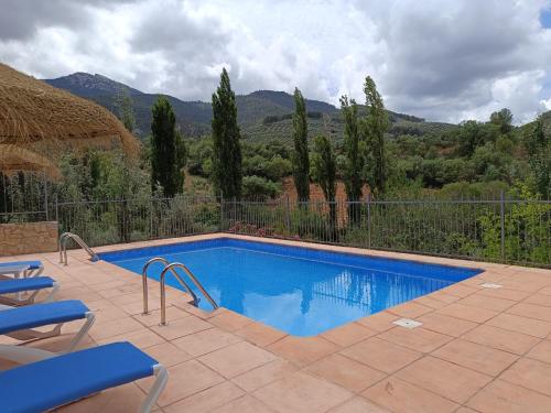 a swimming pool with two blue chairs and a fence at CASA RURAL CURTIDORES in El Batán
