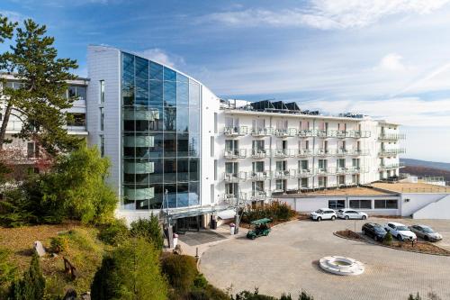 un gran edificio blanco con coches aparcados en un aparcamiento en Hotel Ózon & Luxury Villas en Mátraháza
